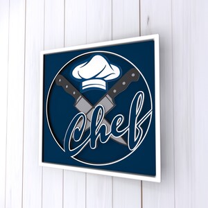 May include: A white framed print with a blue background and a white chef's hat with two crossed knives. The word "chef" is written in a stylized font.