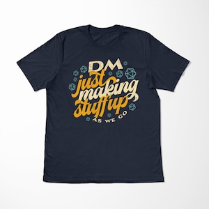 May include: A navy blue t-shirt with a yellow and white graphic that says "DM just making stuff up as we go" with a design of dice around the text.