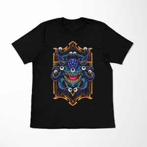May include: Black t-shirt with a graphic of a blue, multi-eyed monster with a toothy grin. The monster is surrounded by a gold frame with intricate details.