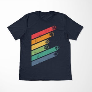 May include: Navy blue t-shirt featuring a retro design with colorful diagonal stripes and geometric dice shapes. The design includes red, orange, yellow, green, and blue stripes, with dice illustrations. A vintage-style graphic tee for tabletop gamers.