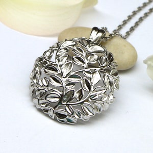 May include: Silver pendant necklace featuring a delicate, intricate design of leaves. The pendant is round and hangs from a silver chain.