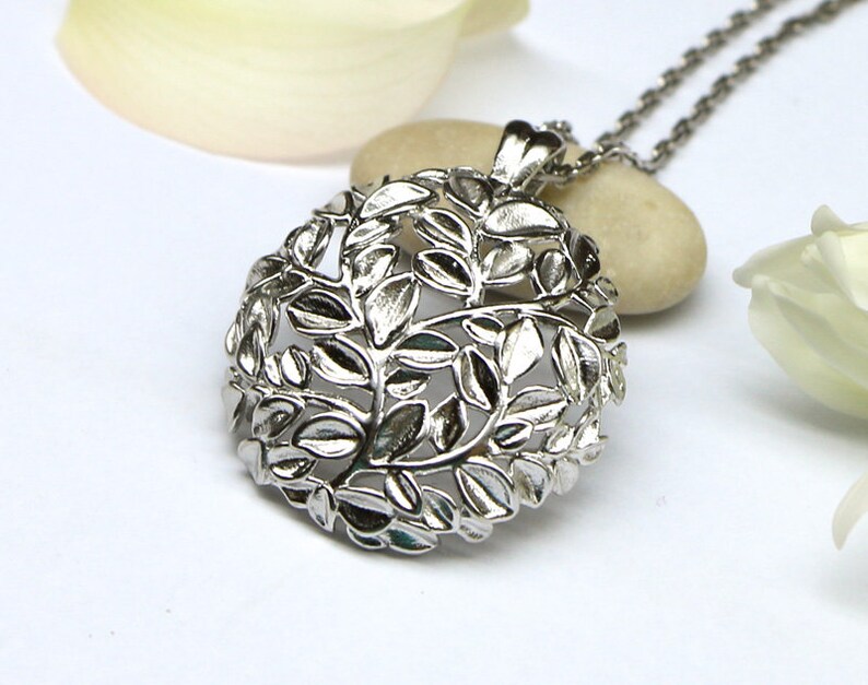 May include: Silver pendant necklace featuring a delicate, intricate design of leaves. The pendant is round and hangs from a silver chain.