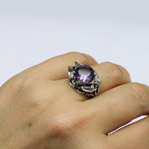 May include: A silver ring with a large, round, purple gemstone set in a detailed, floral design.
