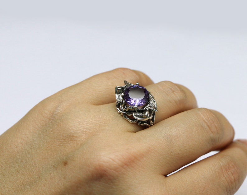 May include: A silver ring with a large, round, purple gemstone set in a detailed, floral design.