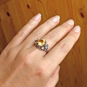 May include: A silver ring with a large, round, yellow gemstone set in a floral design.