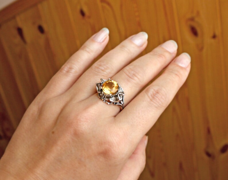 May include: A silver ring with a large, round, yellow gemstone set in a floral design.