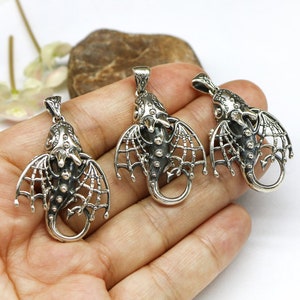 May include: Three silver dragon pendant charms with intricate details and openwork wings. The charms are shown on a hand, ready to be added to a necklace or bracelet.