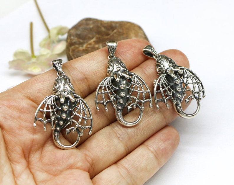May include: Three silver dragon pendant charms with intricate details and openwork wings. The charms are shown on a hand, ready to be added to a necklace or bracelet.