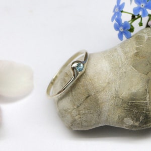 May include: A silver ring with a small blue gemstone set in a wave-like design.