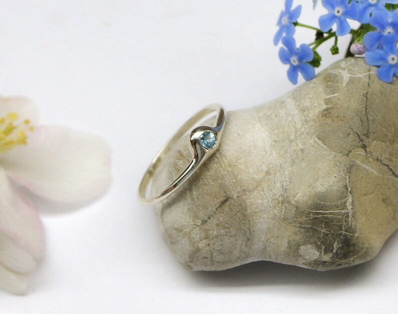 May include: A silver ring with a small blue gemstone set in a wave-like design.