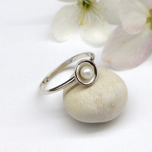 May include: A silver ring with a small white pearl set in a circular design.