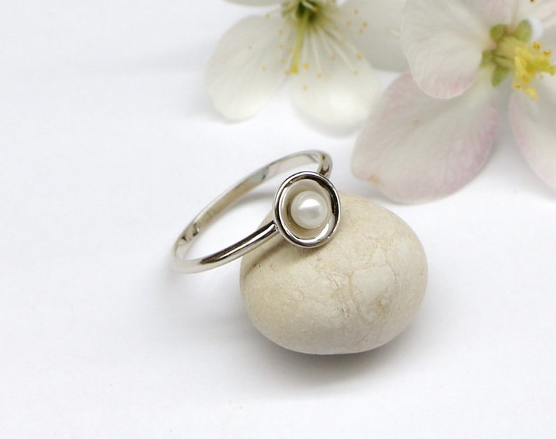 May include: A silver ring with a small white pearl set in a circular design.