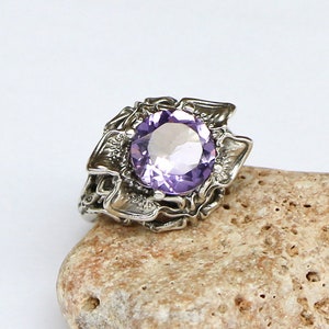May include: A silver ring with an intricate design featuring a large, round, purple amethyst gemstone.