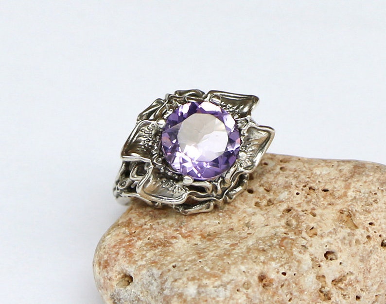 May include: A silver ring with an intricate design featuring a large, round, purple amethyst gemstone.