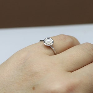 May include: A silver ring with a single white pearl set in a circular design.