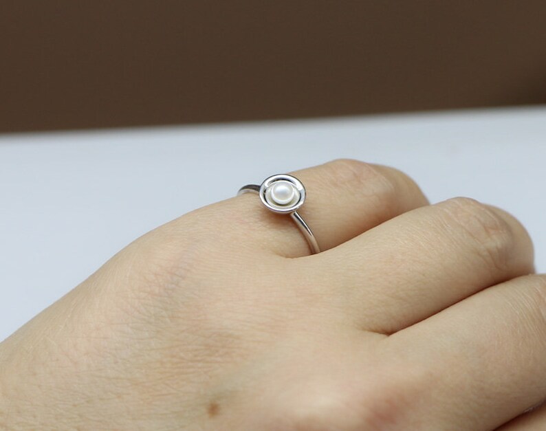 May include: A silver ring with a single white pearl set in a circular design.