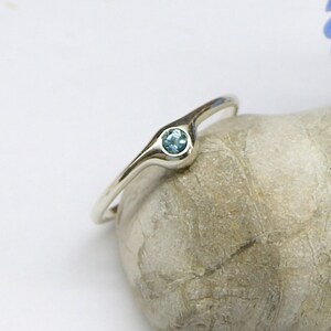 May include: A silver ring with a light blue gemstone set in a curved band.