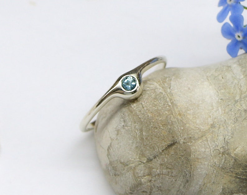 May include: A silver ring with a light blue gemstone set in a curved band.