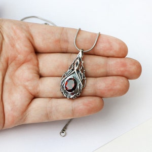 May include: A silver necklace with a red gemstone pendant. The pendant is a detailed design of a tree with a red gemstone in the center.