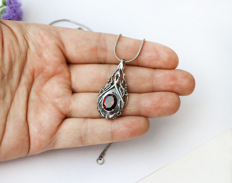 May include: A silver necklace with a red gemstone pendant. The pendant is a detailed design of a tree with a red gemstone in the center.
