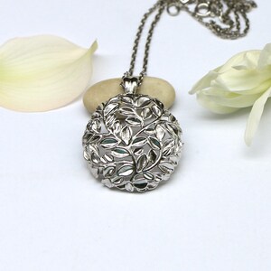May include: A silver necklace with a delicate pendant featuring a circular design of leaves and branches.