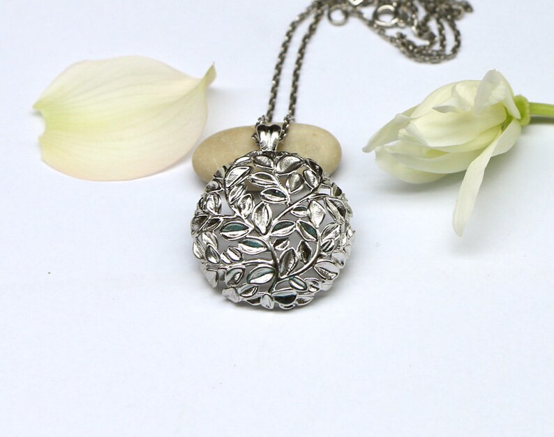 May include: A silver necklace with a delicate pendant featuring a circular design of leaves and branches.