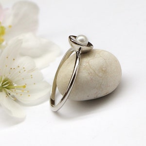 May include: A delicate silver ring with a small white pearl set in a cup-shaped design.