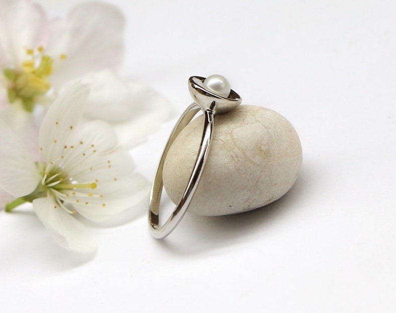 May include: A delicate silver ring with a small white pearl set in a cup-shaped design.