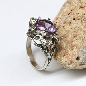 May include: A silver ring with an intricate floral design and a large oval amethyst gemstone.