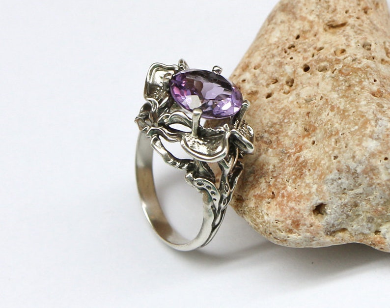 May include: A silver ring with an intricate floral design and a large oval amethyst gemstone.