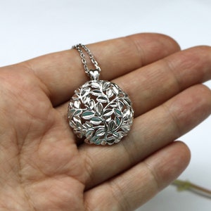 May include: A silver pendant necklace with a circular design featuring a delicate, intricate pattern of leaves. The pendant is suspended from a silver chain.