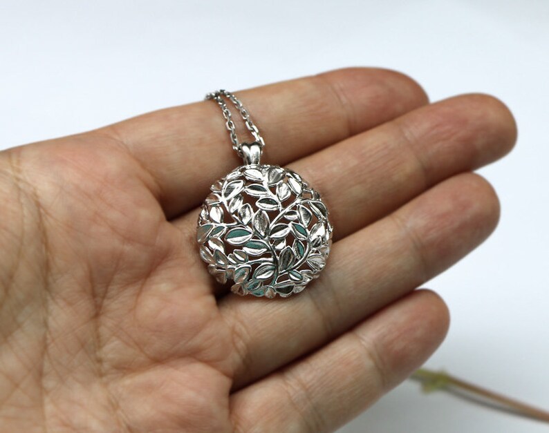 May include: A silver pendant necklace with a circular design featuring a delicate, intricate pattern of leaves. The pendant is suspended from a silver chain.