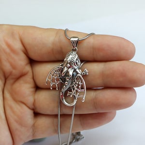 May include: Silver dragon pendant necklace with intricate details and a black stone in the center. The dragon is curled up with its wings spread out.