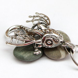 May include: A silver pendant featuring a detailed dragon design with intricate wings and a textured body. The pendant is hanging from a silver chain.