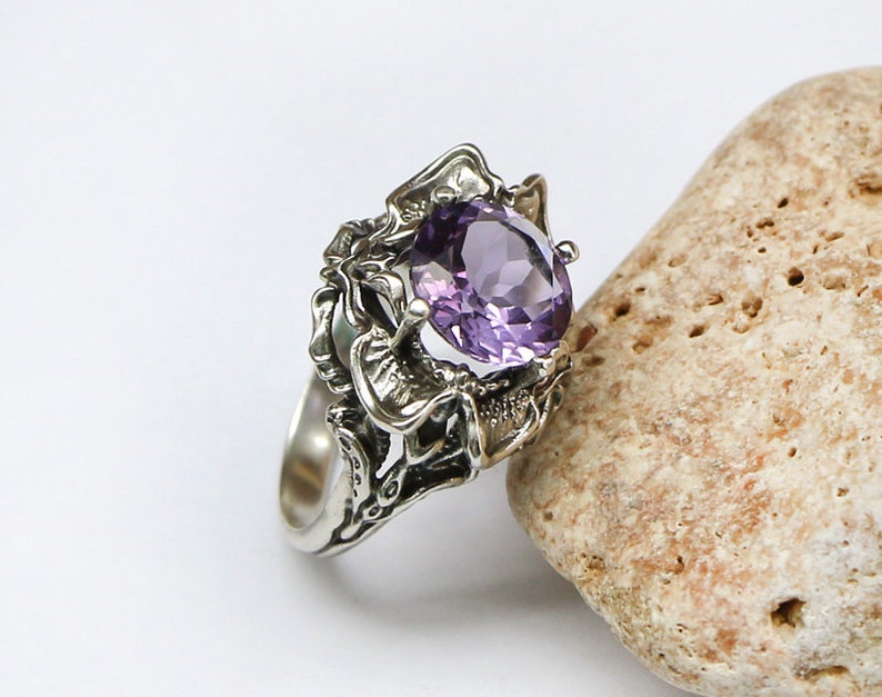 May include: A silver ring with an intricate design featuring a large, oval-shaped amethyst gemstone.