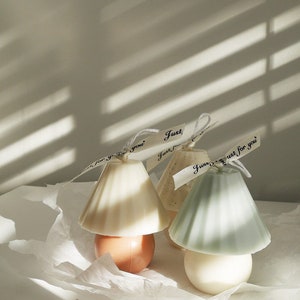Peut inclure: Trois bougies décoratives en forme d'abat-jour avec une base ronde. Les bougies sont dans des tons beige, brun clair et vert clair. Les bougies sont décorées d'un ruban blanc et du texte "Just for you".