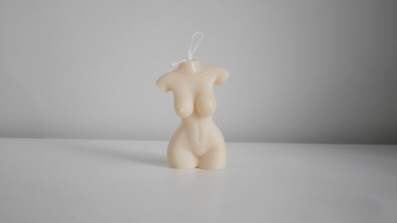 Peut inclure: Une bougie beige en forme de torse f&eacute;minin. La bougie a une surface lisse et est d&eacute;taill&eacute;e pour repr&eacute;senter la forme d'un corps humain. Une m&egrave;che blanche d&eacute;passe du haut. C'est un objet d&eacute;coratif.