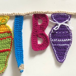 Divertida guirnalda de regreso a clases, con letras, conos escolares y bolígrafos, tejida a crochet con lana