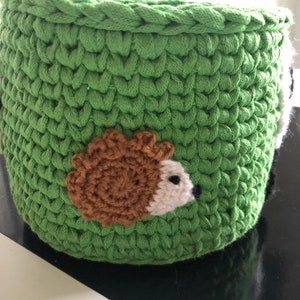 K&ouml;nnte beinhalten: Gr&uuml;ner H&auml;kel-Aufbewahrungskorb mit einem braunen und wei&szlig;en Igel-Applikationen.