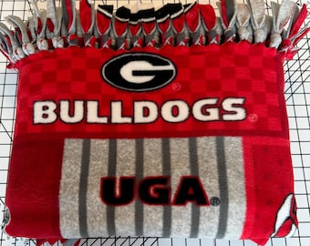 May include: Red and gray fleece blanket with a checkered pattern and the words "Bulldogs" and "UGA" in white and black lettering. The blanket has a gray fringe around the edges.