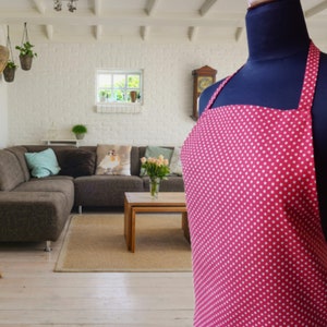 A red and white polka dot apron with straps. The apron is hanging on a black mannequin.