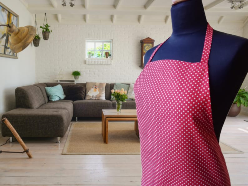 A red and white polka dot apron with straps. The apron is hanging on a black mannequin.