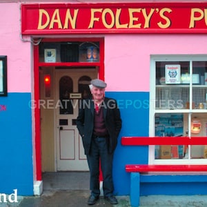 May include: A pink building with a red sign that reads "Dan Foley's Pub". A man in a brown jacket and a flat cap stands in front of the building. The building has a blue door and a window with a sign that reads "Guinness is good for you".