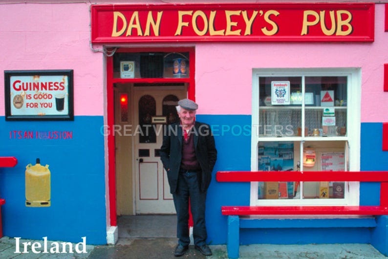 May include: A pink building with a red sign that reads "Dan Foley's Pub". A man in a brown jacket and a flat cap stands in front of the building. The building has a blue door and a window with a sign that reads "Guinness is good for you".