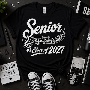 May include: Black t-shirt with "Senior Class of 2027" in white script and musical notes. Accessories include a water bottle, notebook, graduation cap, and sneakers. The theme is graduation.
