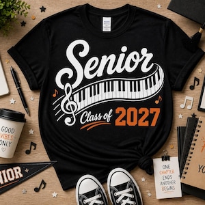 May include: Black t-shirt with a white "Senior" design featuring a piano keyboard and musical notes, with "Class of 2027" in orange. Accessories include a notebook, headphones, and a pennant.