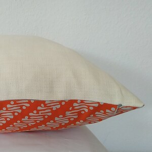 May include: A white pillow with a zipper closure. The pillow has an orange and white patterned fabric on the bottom edge.