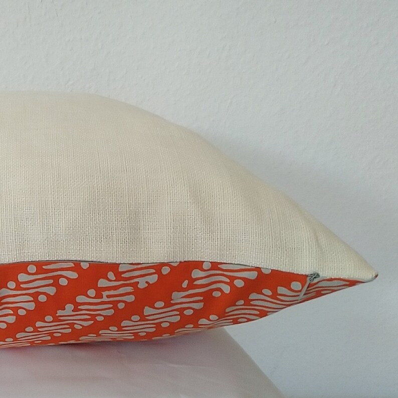 May include: A white pillow with a zipper closure. The pillow has an orange and white patterned fabric on the bottom edge.