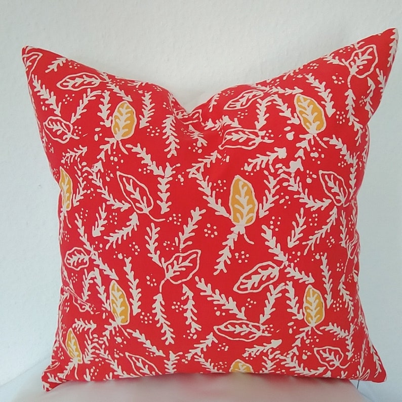 Pu&ograve; includere: Cuscino rosso con un motivo floreale bianco e giallo.