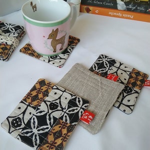 Peut inclure: Quatre sous-verres avec un motif géométrique noir et blanc. Un sous-verre est en tissu de lin naturel. Les sous-verres ont une étiquette rouge avec le texte "@Home" dessus.